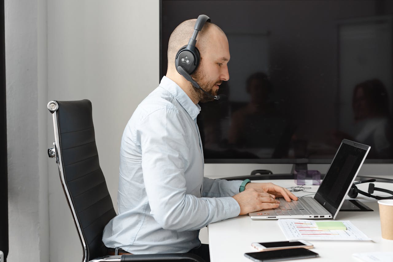 A focused call center agent with headphones working on a laptop in an office.